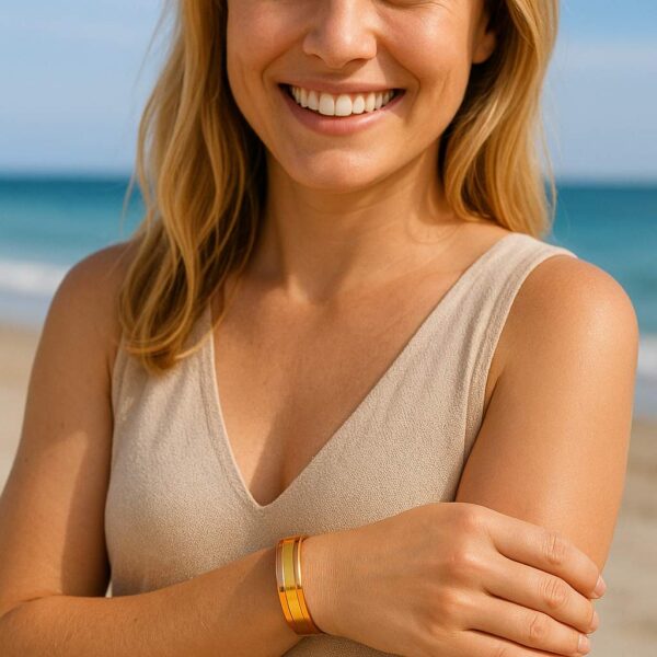 Lachende Frau am Strand trägt ein breites Kupferarmband mit goldfarbenem Messingstreifen und zwei Neodym-Magneten am Handgelenk.
